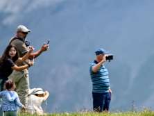 Plusieurs personnes se tiennent dans une prairie d'alpage verdoyante et prennent en photo une vache solitaire. La scène illustre la découverte par les visiteurs de l'économie d'alpage traditionnelle.