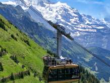 Die Luftseilbahn Wengen–Männlichen schwebt über steilen alpinen Wiesen bergauf. Im Hintergrund erhebt sich die eindrucksvolle Hochgebirgslandschaft und unterstreicht die spektakuläre Lage der Bahn.