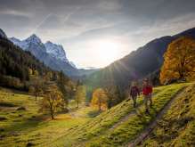 Two hikers are out and about in the Rosenlauital valley. There is an autumnal atmosphere, and the sky is covered with light, hazy clouds. The mountain panorama is blanketed in snow.