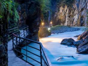 Ambiance du soir dans les gorges de l'Aar. La passerelle qui longe l'eau est éclairée. Sous l'effet de la lumière, les parois rocheuses se teintent d'un jaune apaisant.