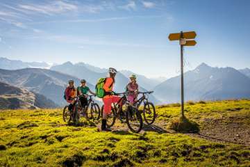 The bikers look at the signpost and enjoy the view from Hasliberg. The view offers a summery panorama of the mountain landscape.