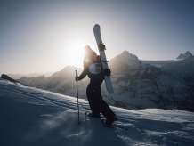 Schneeschuhlaufen auf der First mit einem Snowboard am Rücken in der Morgensonne.