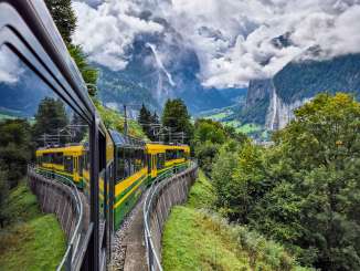 Le téléphérique de la Wengernalp longe un versant à travers une vallée verdoyante. En arrière-plan, la vallée de Lauterbrunnen s'ouvre sur des parois rocheuses escarpées et des sommets imposants, sous un ciel nuageux changeant.