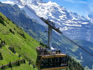 The Wengen–Männlichen aerial tramway glides uphill over steep alpine meadows. In the background, the impressive high-mountain landscape rises up, highlighting the tramway’s spectacular location.