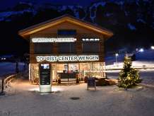 Das Tourist Center ist hell beleuchtet an einem Winterabend in Wengen. Ein beleuchteter Weihnachtsbaum steht vor dem Haus.