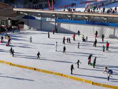 ie grossflächige Eisbahn in Wengen ist von zahlreichen Eisläuferinnen und Eisläufern belebt. Auf der Eisfläche bewegen sich Kinder und Erwachsene, während am Rand Zuschauer stehen und sich vorbereiten. Im Hintergrund sind Dorfgebäude sowie weitere Wintersportanlagen zu sehen.