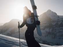 Schneeschuhlaufen auf der First mit einem Snowboard am Rücken in der Morgensonne. 