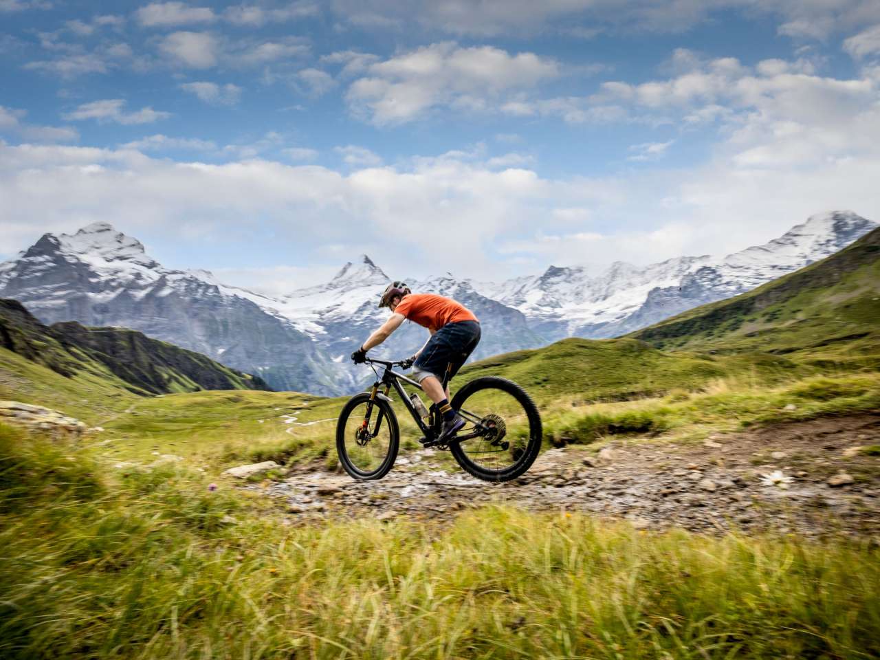 Un cycliste vêtu d'un t-shirt rouge descend la montagne, avec en arrière-plan le panorama montagneux de Grindelwald.