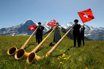 At the Mountain Spring Festival on the Männlichen, three musicians are playing the alphorn on the meadow.
