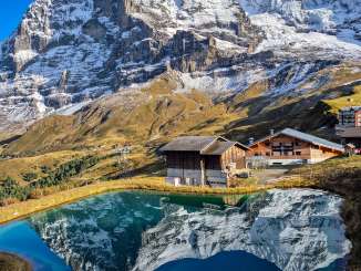 Le restaurant d'altitude de la Petite Scheidegg surplombe un petit lac de montagne. En arrière-plan se dressent l'Eiger et le Mönch, dont les flancs rocheux et enneigés se reflètent dans les eaux calmes.