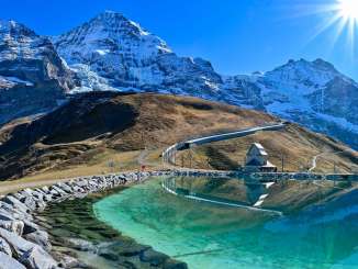 Lake Fallboden near Kleine Scheidegg lies beneath a clear blue sky. In the background rise the Eiger, Mönch, and Jungfrau.