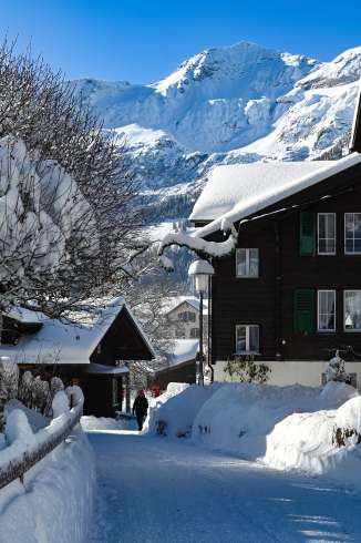 Verschneiter Dorfweg in Wengen zwischen traditionellen Chalets. Im Hintergrund erhebt sich die Jungfrau mit ihren schneebedeckten Flanken unter klarem Himmel