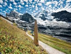 Frühsommerlicher Blick auf die Station der kleinen Scheidegg mit Blick auf die Jungfrau. Die Gletscher bedecken die Berge. Im Vordergrund ist der Wanderweg des Jungfrau Eiger Walk zu sehen.