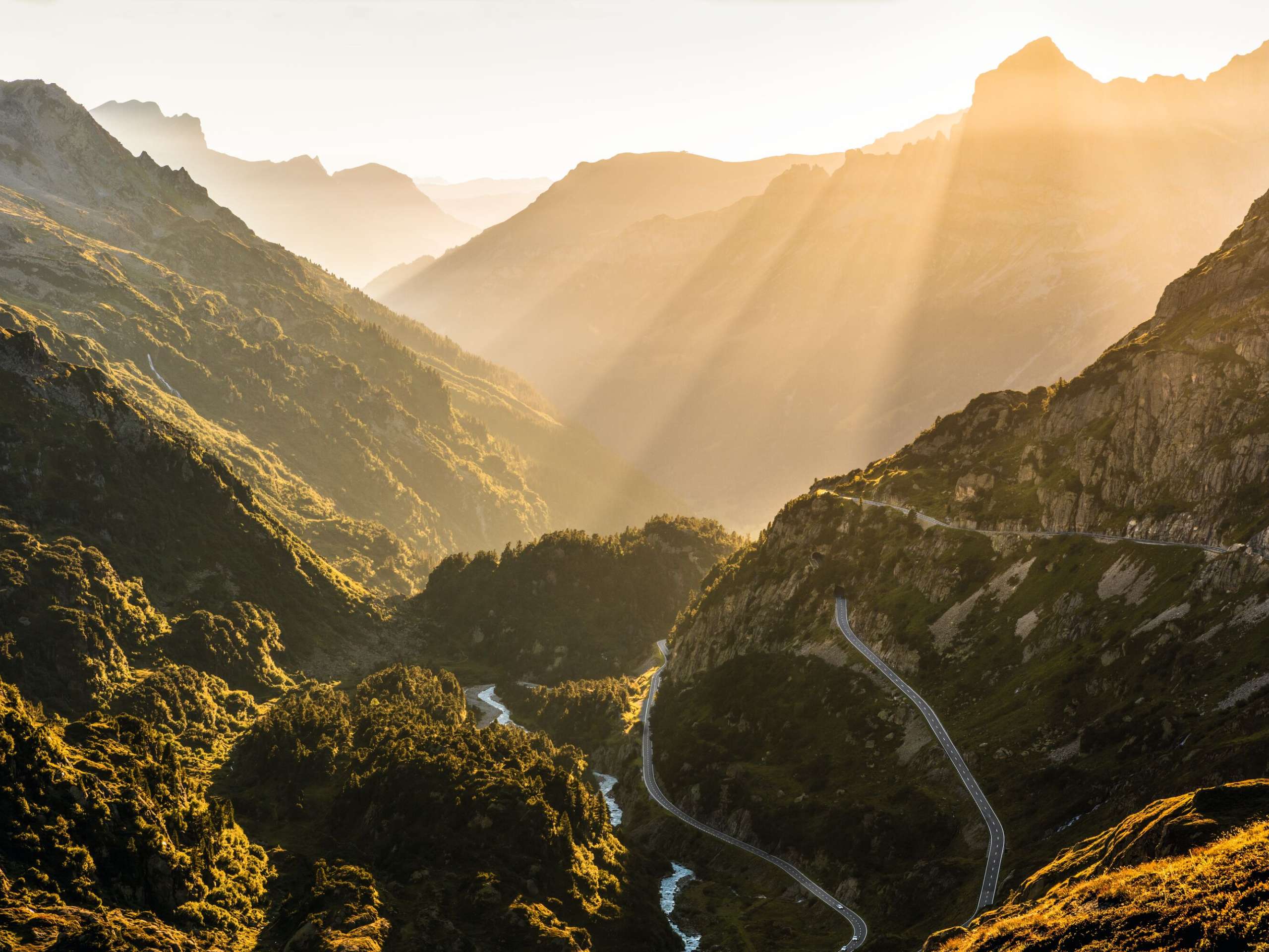 The pass road on the Susten Pass branches off through the rocky landscape overgrown with bushes. The sunlight in the evening lends the landscape a romantic atmosphere.
